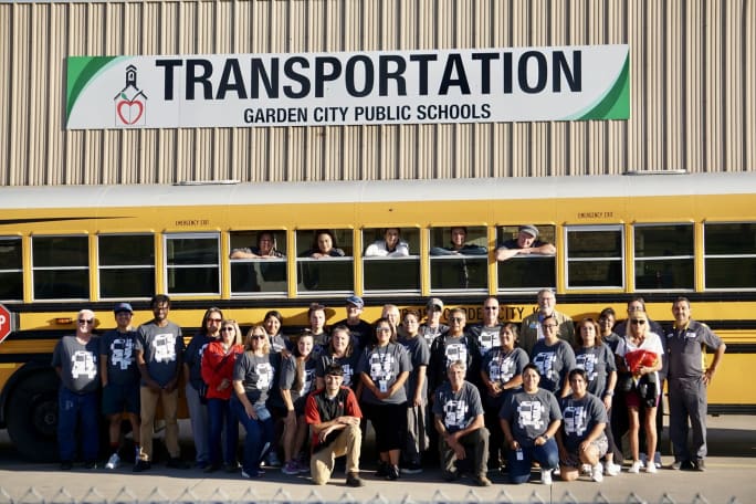 Garden City Public Schools transportation staff pose in front of a school bus outside the district transportation facility in Kansas.