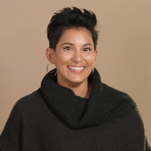 a headshot of a woman wearing a black turtleneck against a tan background
