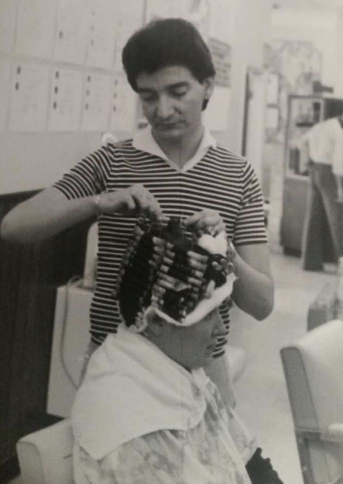 A male hairdresser puts curlers in a woman's hair. 