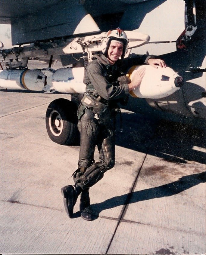 Martin Staples posing against an aircraft in a Naval flight suit and helmet.