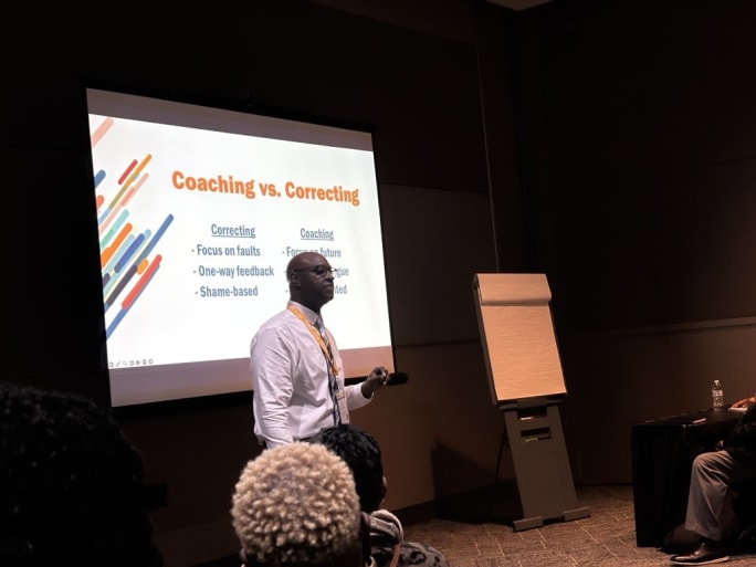 Keith Terry presents to a group session at an NAPT conference with a slideshow on a projector screen behind him.