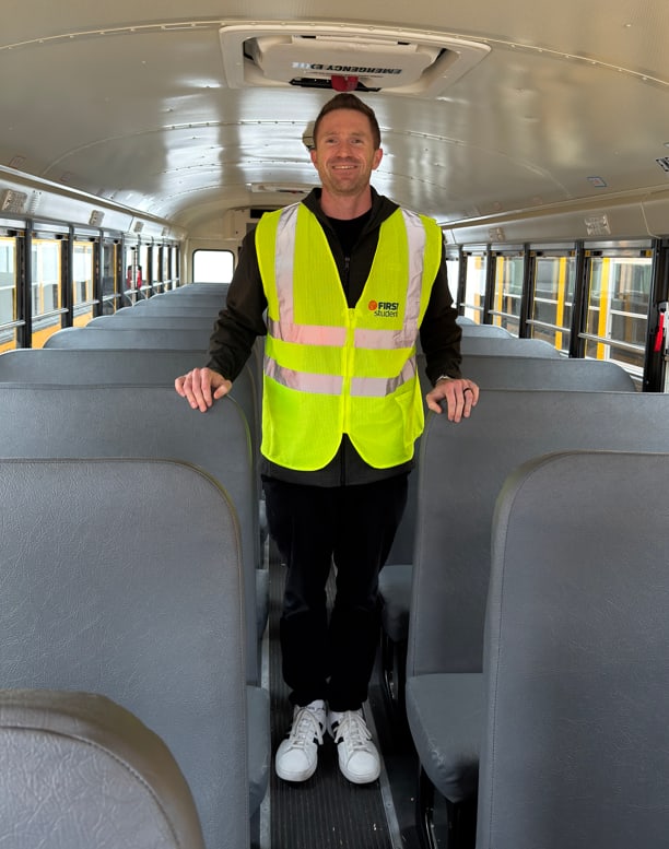a man stands in the aisle of a school bus wearing a yellow safety vest