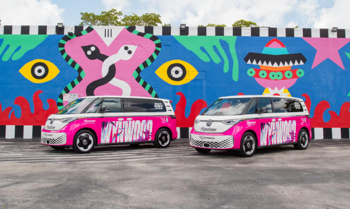Two pink and white Freebee vans parked in front of a mural.