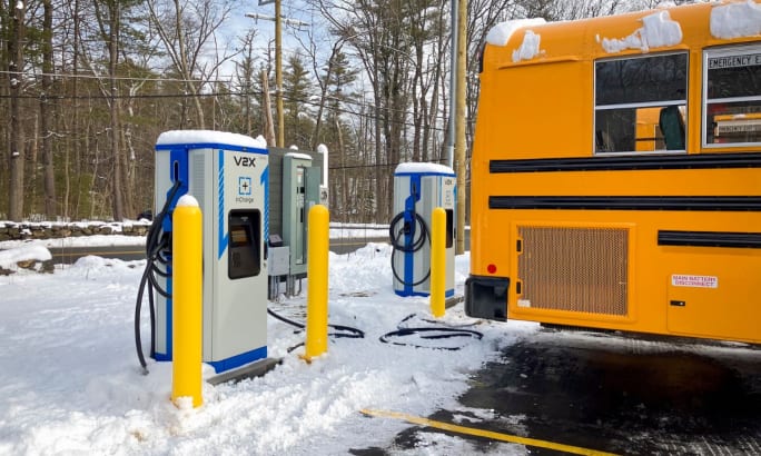 The back end of a school bus next to charging infrastructure surrounded by snow.