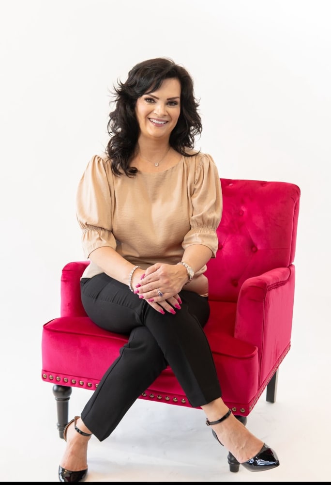 A woman with crossed legs, black hair, wearing slacks, sitting on a red chair.