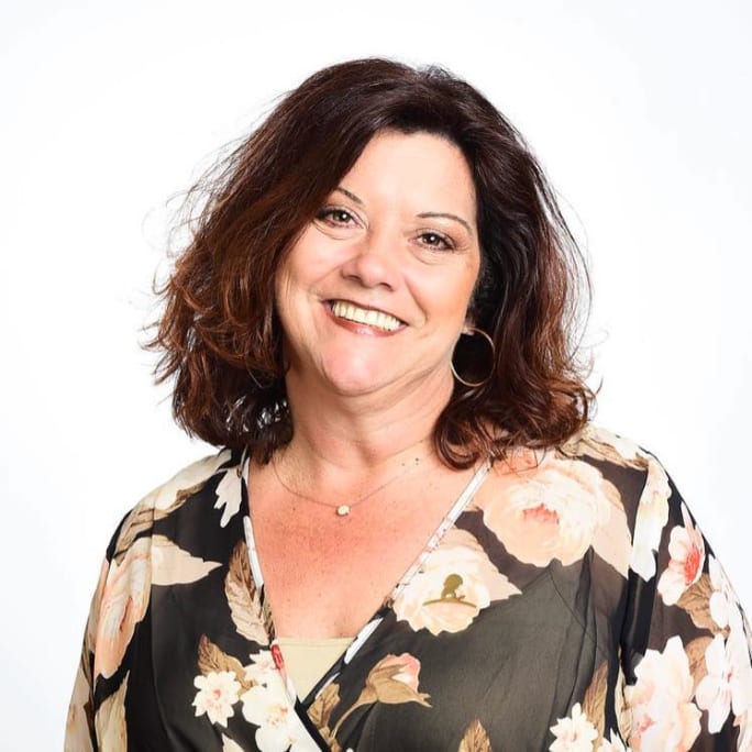 A smiling brunette woman wearing a floral dress. 