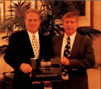 two men stand next to each other in suits for an award presentation