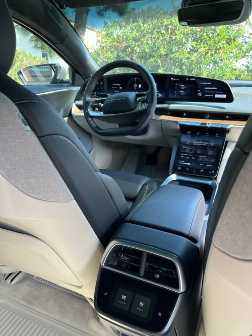 A view from the rear seat of the driver seat, steering wheel, and dashboard of a Lucid Air sedan.