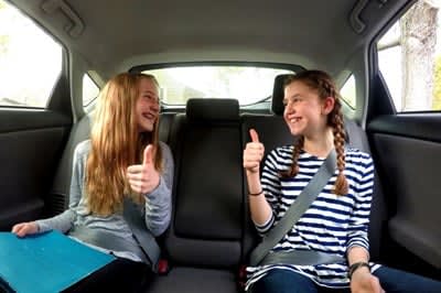  two young girls give eachother the thumbs up signal in the back seat of a car