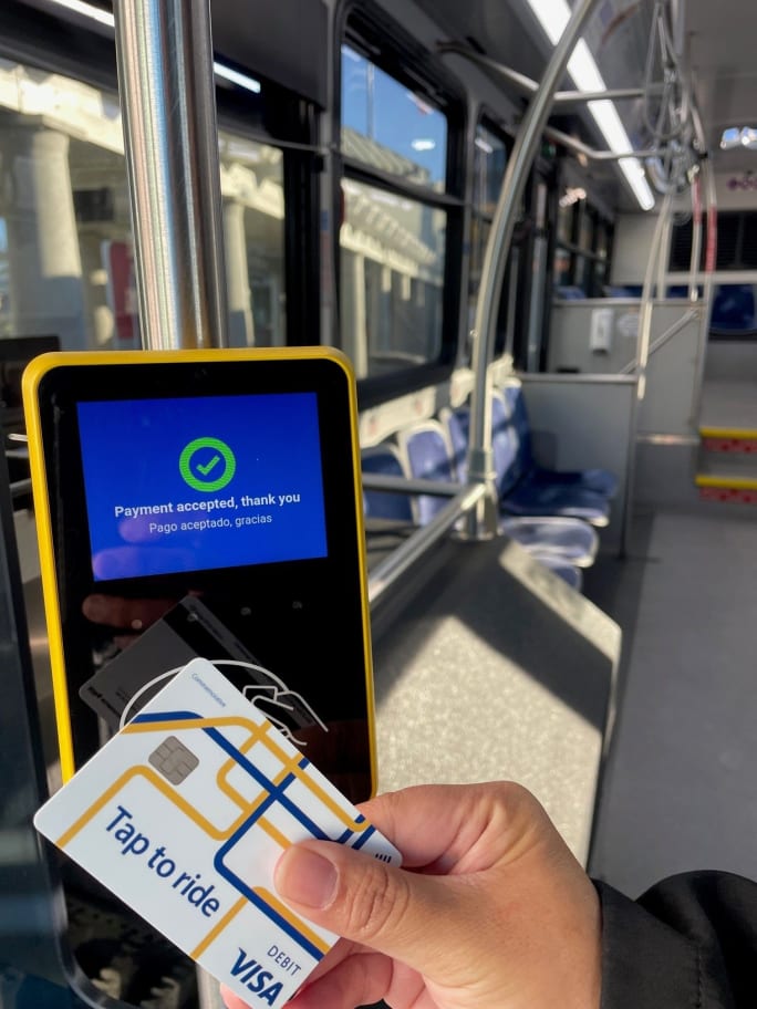 A hand holding a visa card taps an MST fare payment system.