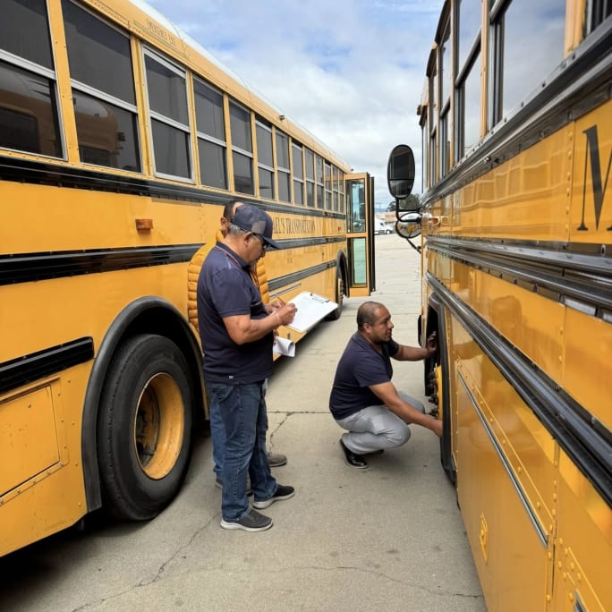 two transportation staff stand by a school bus outside on a but lot during an in-service training