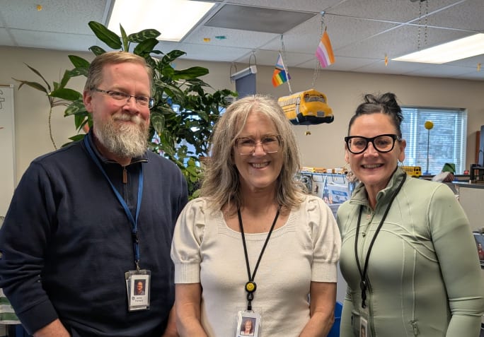 three people stand together in an office 