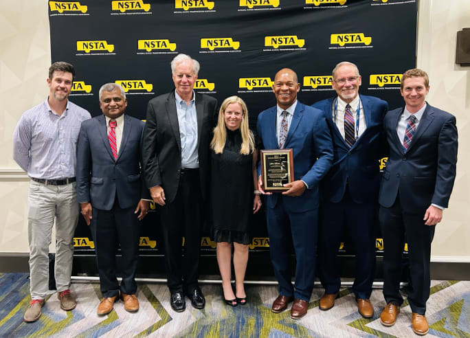 John Elliott Jr. holds the NSTA Golden Merit Award while posing with National School Transportation Association leaders during the awards presentation at an NSTA event.