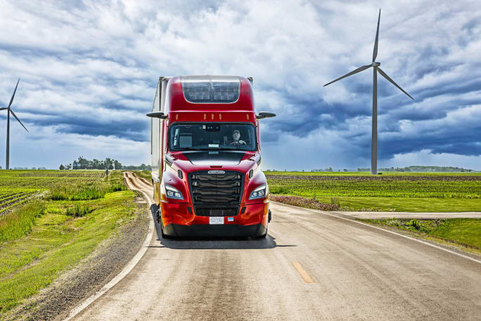 Red Nussbaum tractor going down highway with wind turbines in background