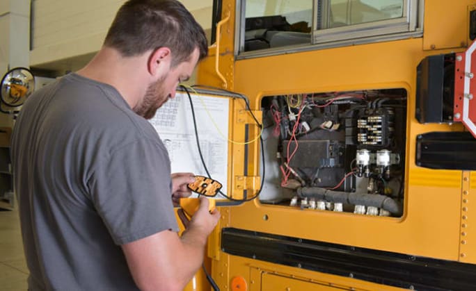 a man checks a school bus panel for maintenance