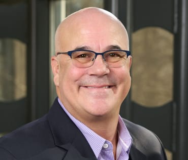 a headshot of a bald man in a black suit
