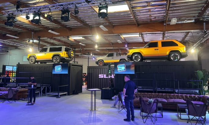 Three yellow-colored Slate models displayed on raised platforms ringed with black curtains.