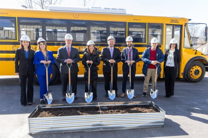 A group of people stand in line with shovels and hard hats at a ground breaking ceremony.