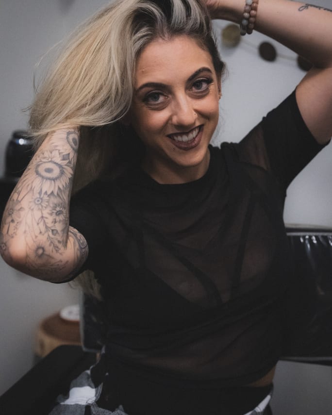 A woman with long hair, her hands in her hair, sitting and smiling.