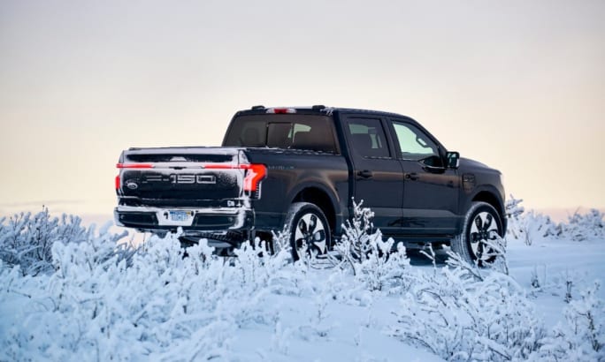 The back right quarter of a black 2022 Ford F-150 Lightning surrounded by a snowy landscape.