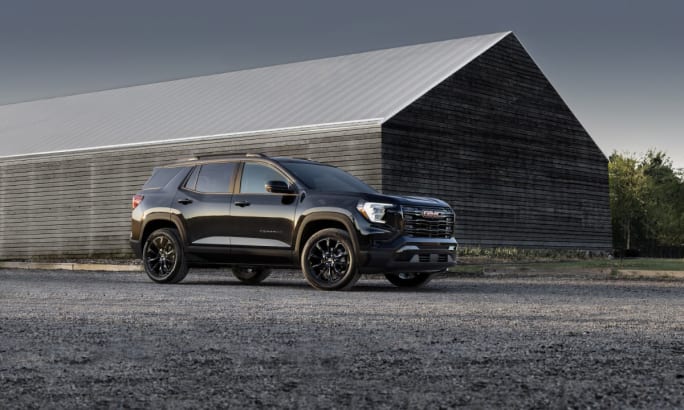 The front right side of a black 2025 GMC Terrain Elevation in front of a metal warehouse.