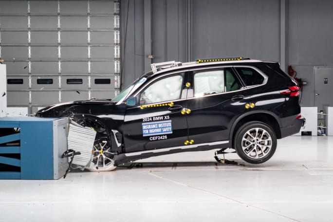 A black BMW X5 in a crash testing room mid-crash.