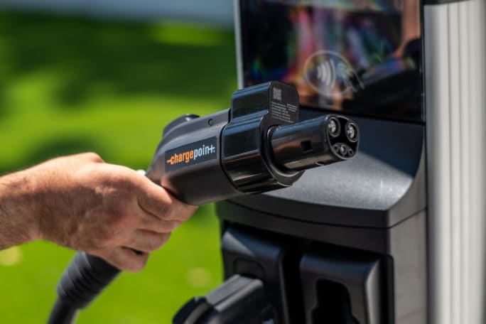 A hand golds out an EV Omni Port charging connector attached to a ChargePoint station.