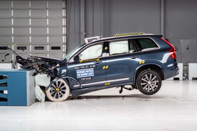 A blue Volvo XC90 in a crash testing room mid-crash.