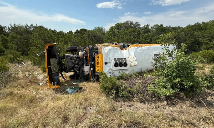 A damaged school bus on its side in an embankment. 