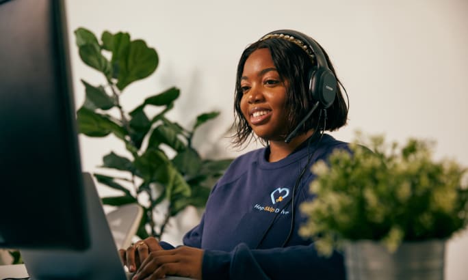 A HopSkipDrive support team member at a computer and talking on a headset.