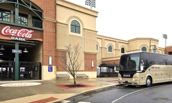 An image of a sports stadium with a Trans-Bridge lines gold motorcoach park in front.