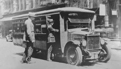 Historical black and white photograph of A.J. Ferraro boarding one of the first makeshift buses.