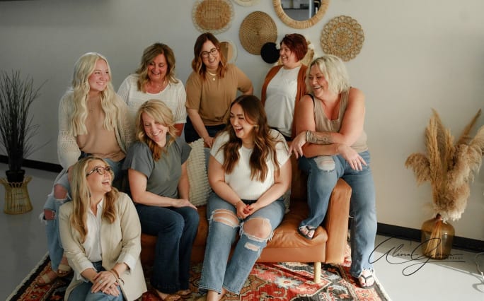 Looking at one another and sharing a laugh, a group of people pose on a tan couch.