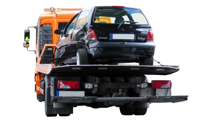 The rear view of a dented minivan on a flatbed tow truck.