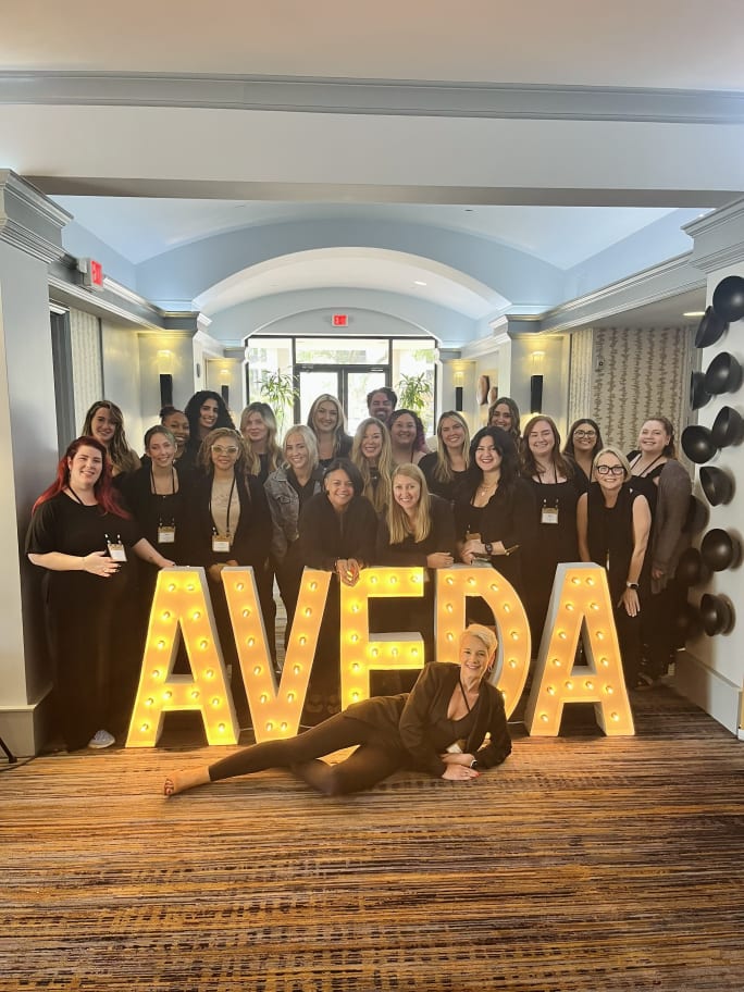 Kelly Weary in front of Aveda Marquee letter with her team behind her.