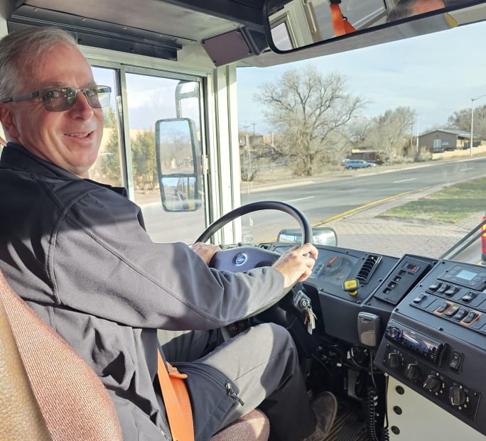 A man sits behind the wheel of a school bus, looking back toward the camera.