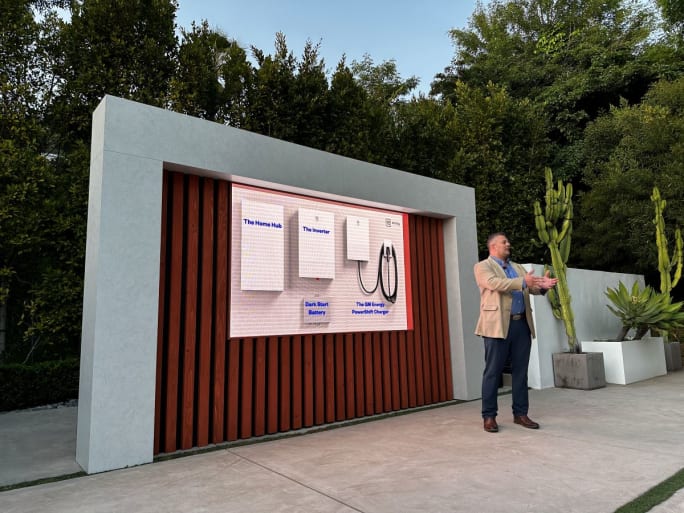 Man stands next to a digital screen at an outside event.