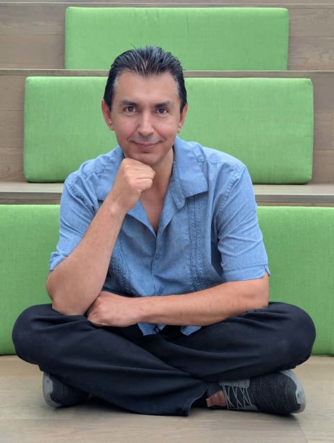 Carlos Bazan is sitting cross-legged in front of light green paneled steps.