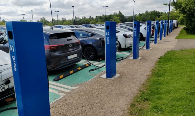 A back view of a row of electric vehicles lined up at parking lot chargers.