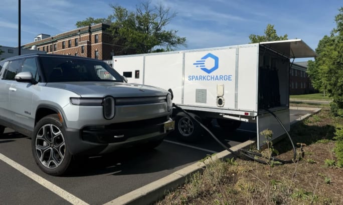 A Rivian SUV charging from a SparkCharge mobile rectangular charger.