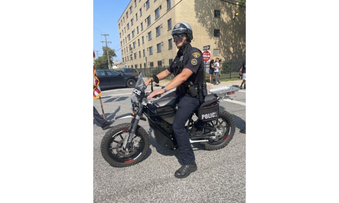 An officer poses on a silver and black e-bike called The District during a test run of the bike.