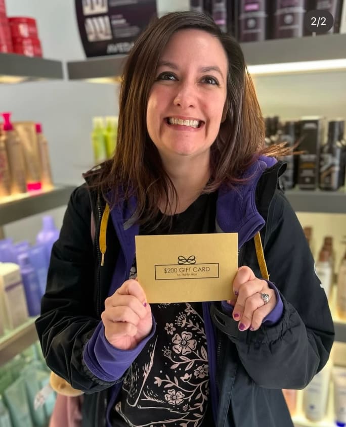 Smiling Thirty Hair client holding a gift card prize, representing a holiday retention program that encourages rebooking and repeat visits during slower months.