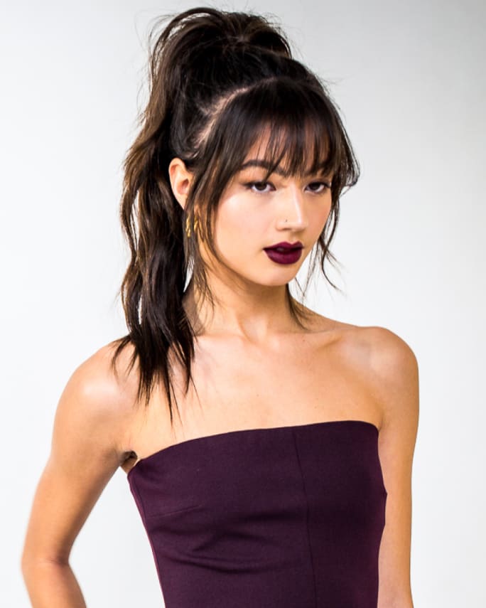 a woman in dark lipstick, a dark tube top and a high ponytail posing