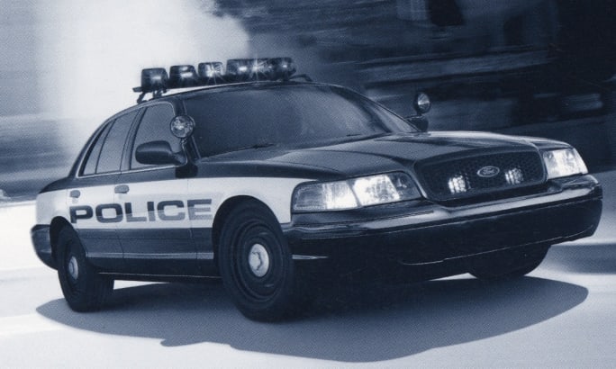 Black and white police patrol car in motion with emergency lights