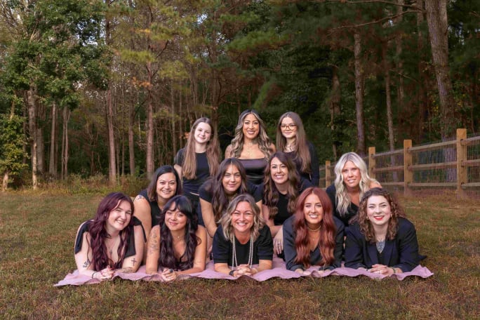 A group of stylist in a pyramid formation on top of pink towels in a forest setting.