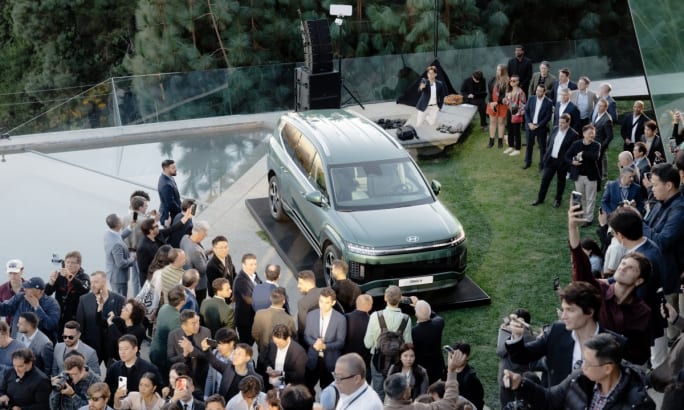 An aerial view of a green Hyundai Ioniq 9 is parked amidst a crowd of people.