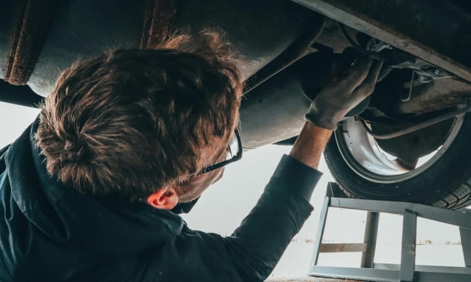 An auto mechanic checking the undercarriage of a car.