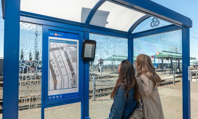Two women look at ePaper digital signage at a bus stop.