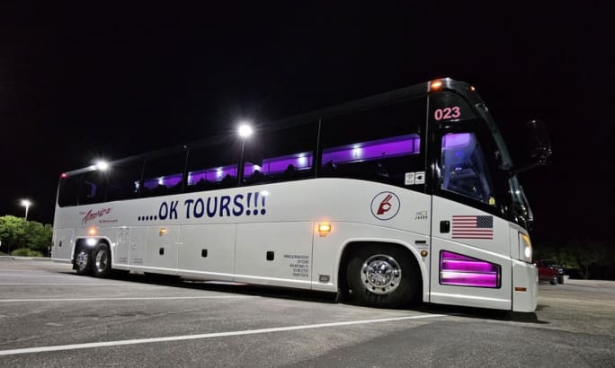 A white, black, and purple OK TOURS motorcoach at night.