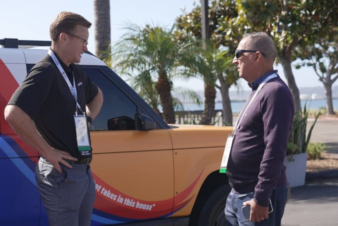 A sales rep talks to a customer in front of a brightly colored electric vehicle prototype.